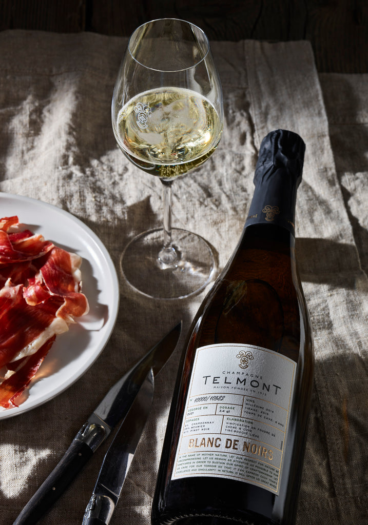 A lifestyle photo of a bottle Blanc de Noirs lying close to a place with dry ham